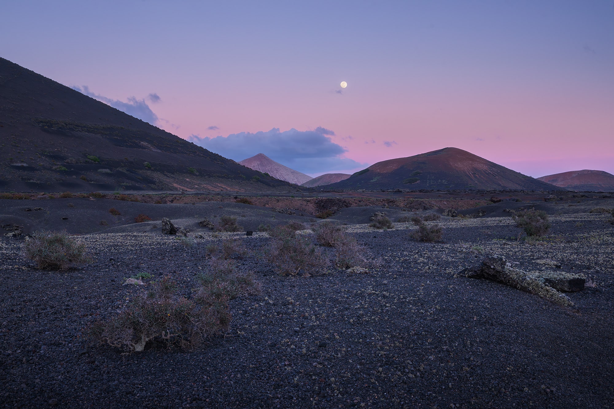 Wide-angle landscape photography of the moon rise at blue hour near Volcán del Cuervo in Lanzarote, showcasing volcanic landscapes and soft twilight hues in the Canary Islands.