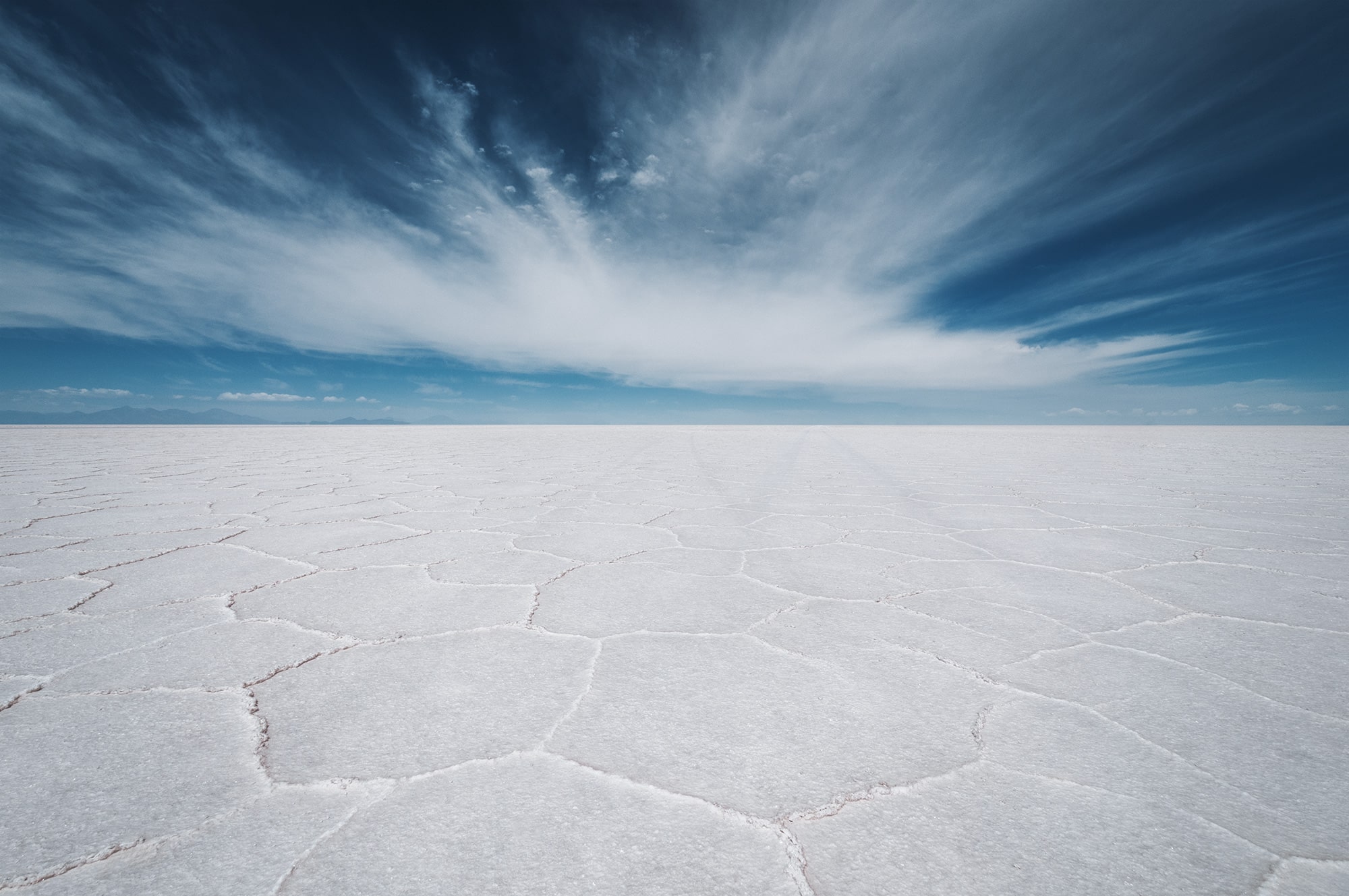 Landscape photography of the Salar de Uyuni, the Bolivian salt flats in Latin America, showing white salt hexagons on the ground under a vivid blue sky with clouds, captured in the high-altitude Altiplano of Bolivia.