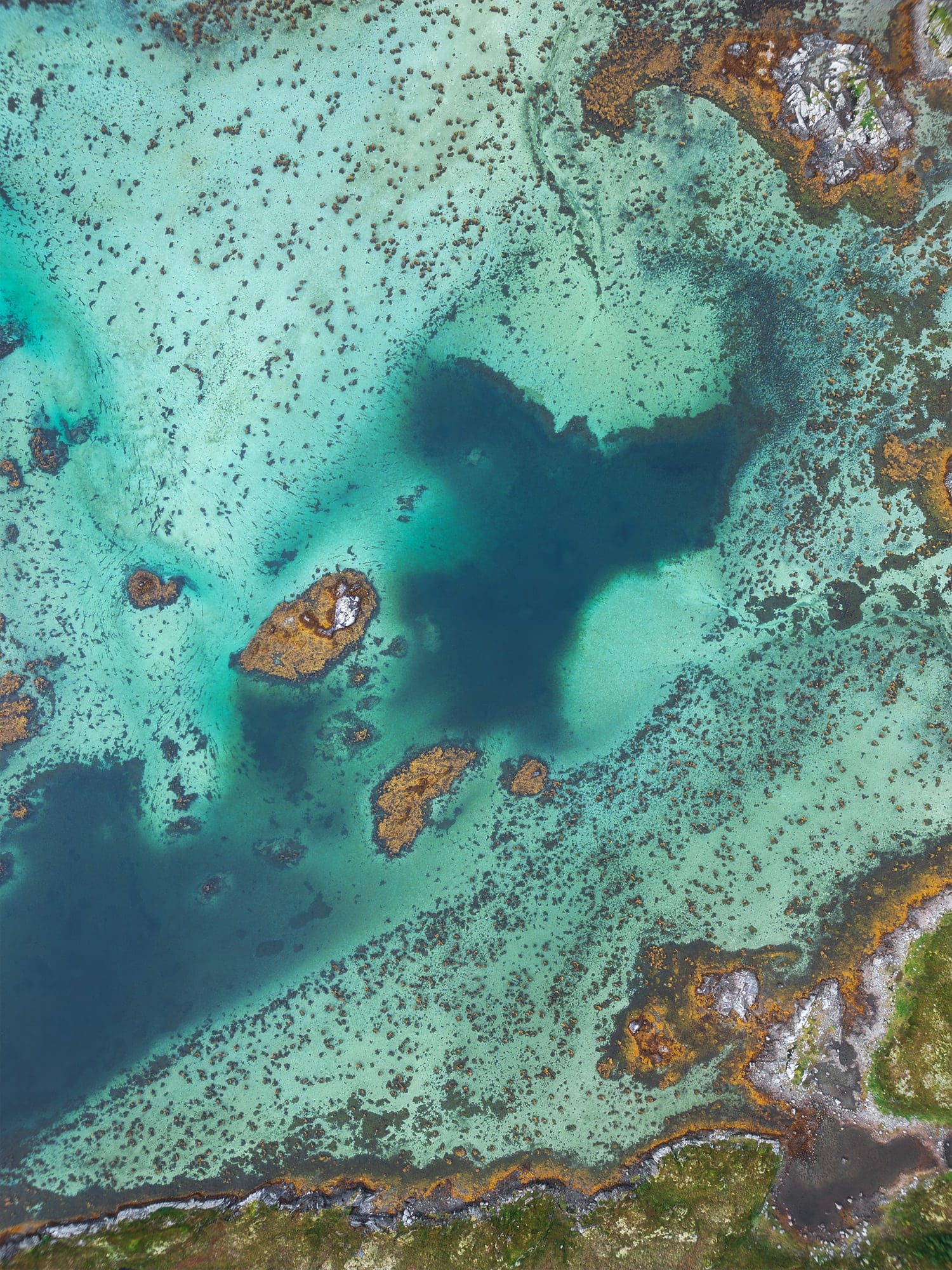 Drone photography of the turquoise waters of Gimsøystraumen near Henningsvær in the Lofoten Islands, Norway, captured from above with abstract patterns formed by currents, seaweed, and rocky shallows.