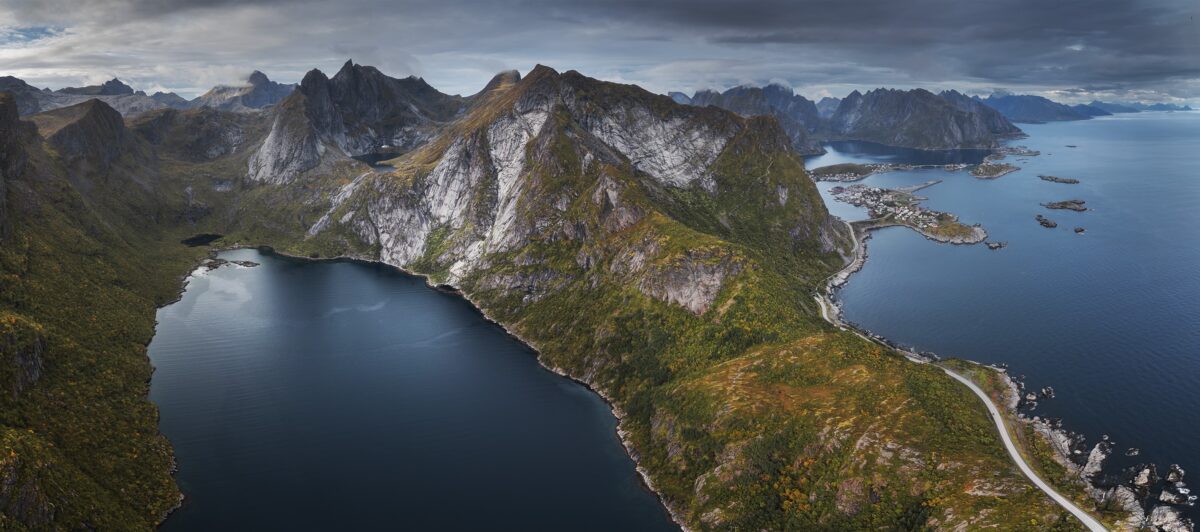 Panoramic drone landscape photography of the southern Lofoten coastline, capturing the mountain range around Djupfjorden and Reine, Norway, with dramatic Arctic scenery seen from above.
