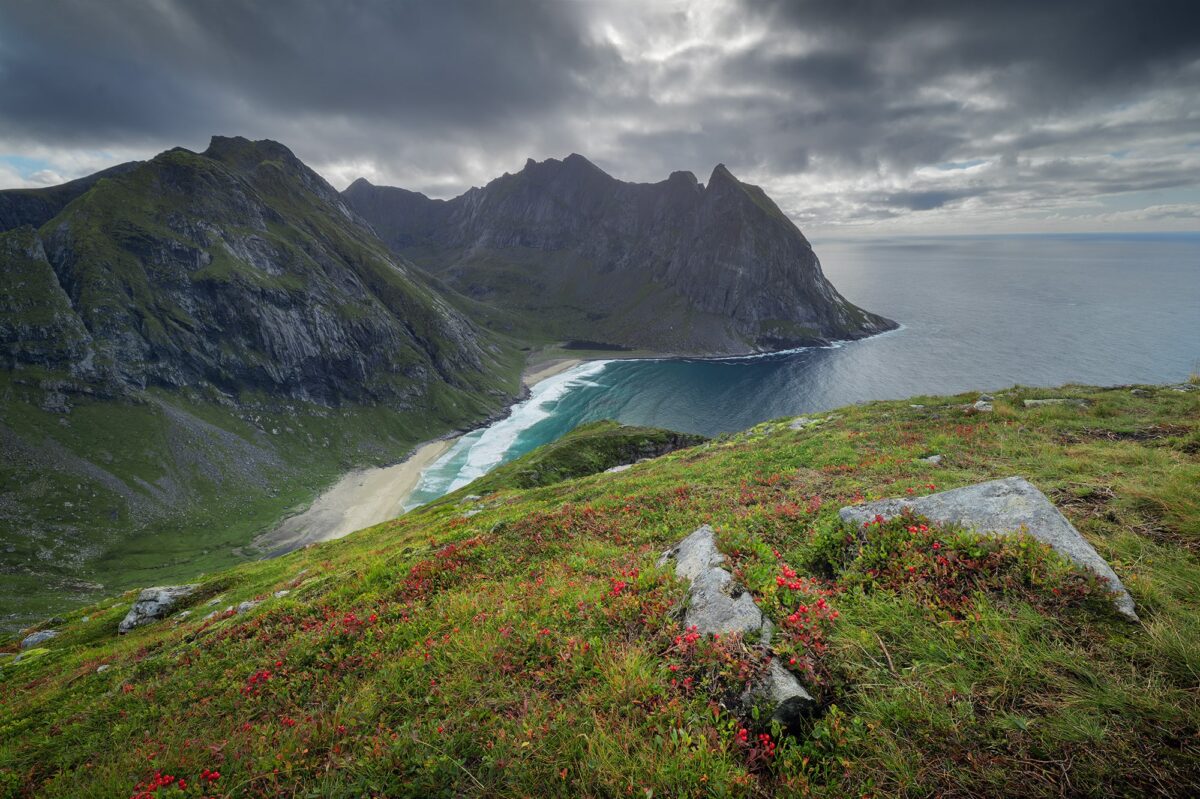 Landscape photography of Kvalvika Beach seen from the Ryten viewpoint in the Lofoten Islands, Norway, with dramatic cloud coverage and a wild, rugged Arctic landscape.