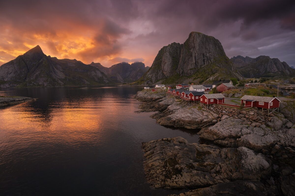 Landscape photography of Hamnøy fishing village in the Lofoten Islands, Norway, captured at sunset with a fiery sky and glowing orange clouds above the iconic Arctic coastline.