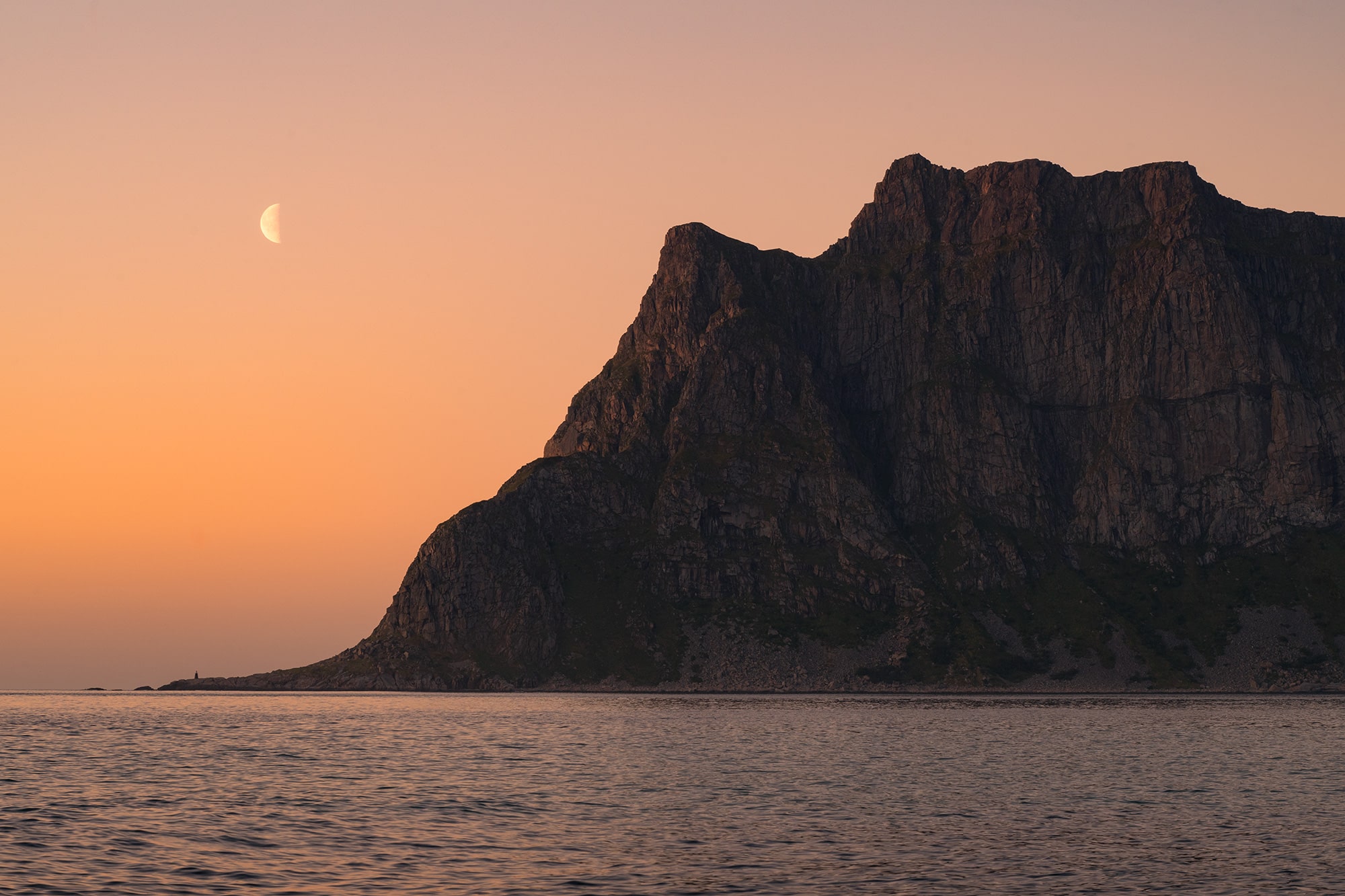 Landscape photography of a moonrise at sunset at Uttakleiv Beach in the Lofoten Islands, Norway, with the full moon rising above the rugged mountain range along the Arctic coast.