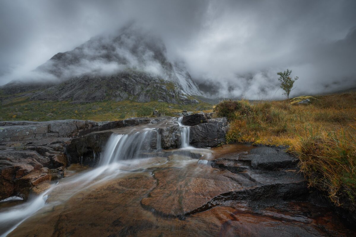Landscape photography of Molneva-fossen waterfall in the Lofoten Islands, Norway, captured on a moody and foggy day with a semi-long exposure, creating a soft and atmospheric scene.