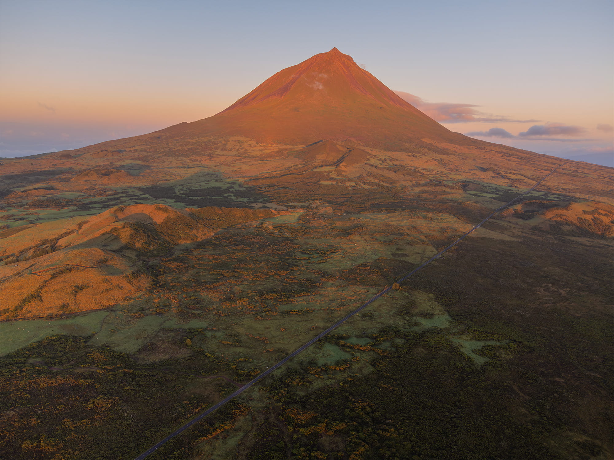 Drone view of Lagoa do Capitão at sunrise with Mount Pico in the background, taken on Pico Island in the Azores. The soft morning light reveals the lake’s reflections and the volcanic peak.