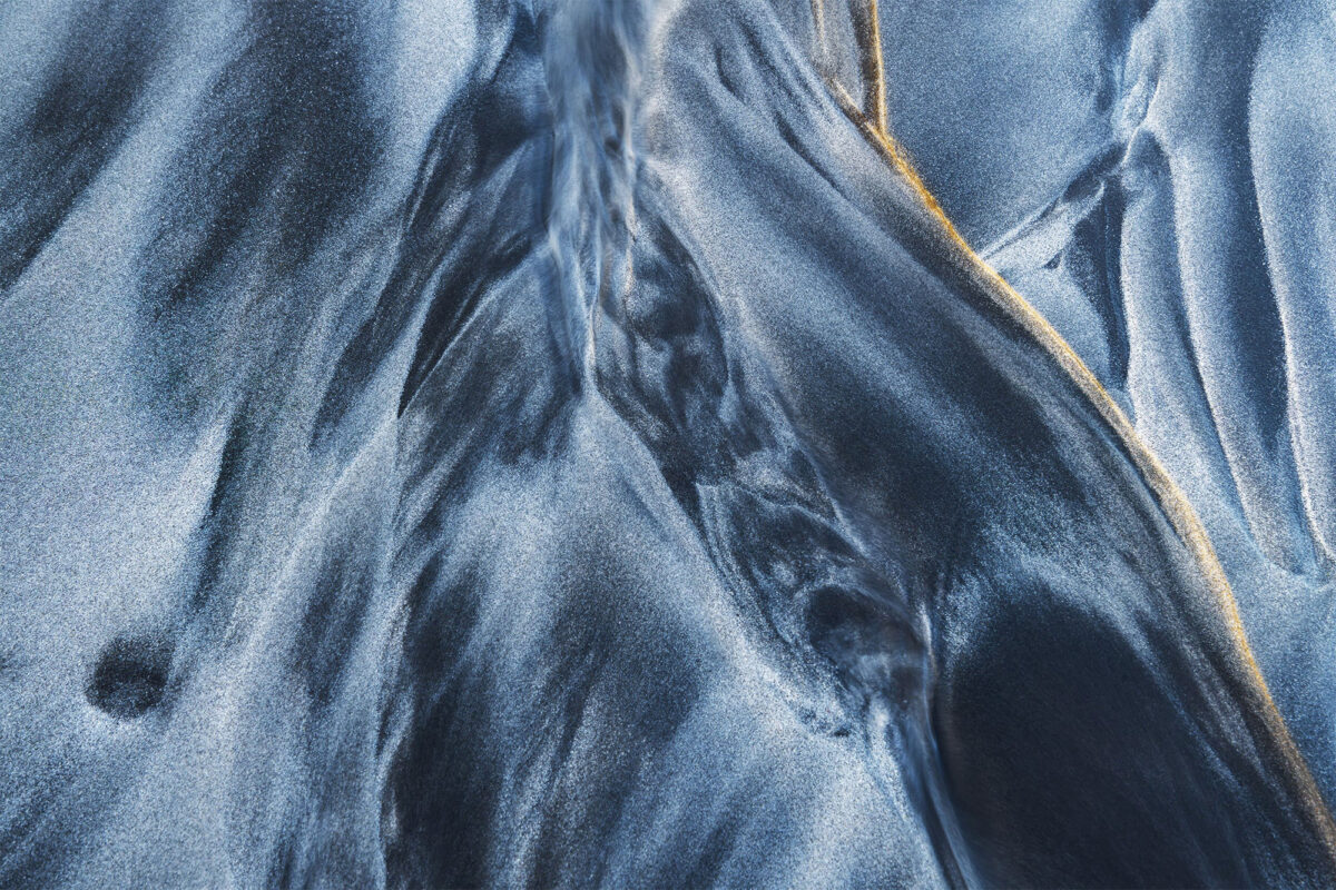 Close-up of abstract black sand patterns with golden line at Skagsanden Beach in the Lofoten Islands, Norway, captured at low tide in autumn light.