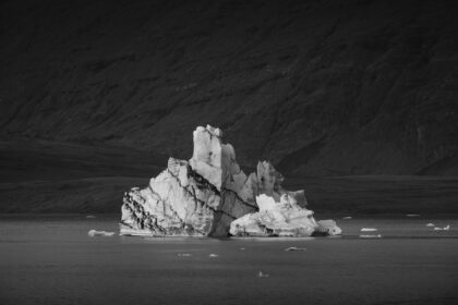 Black and white photograph of an iceberg floating in Jökulsárlón glacier lagoon, Iceland, with strong contrast between ice, dark water and rocky background.