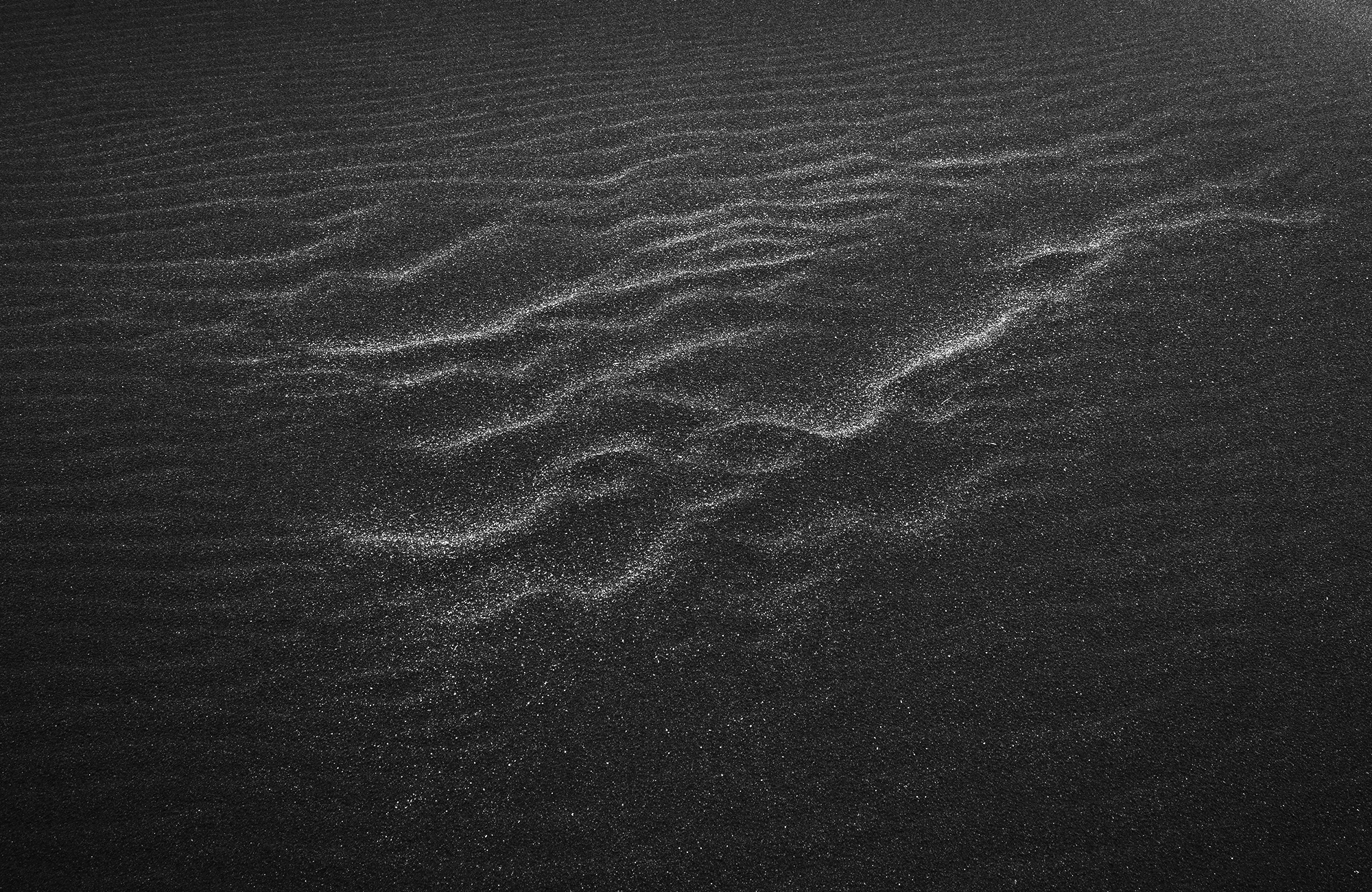 Black and white photograph of wind-shaped sand patterns on Stokksnes beach, Iceland, revealing subtle textures and flowing lines across the dark volcanic sand.