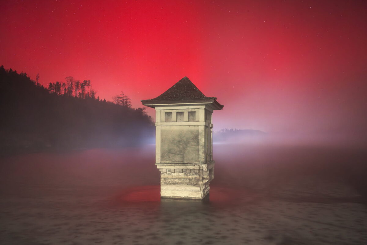 Landscape photography of a red aurora borealis with a lot of fog in Switzerland, captured on January 19, 2026, at Lac de Bret in Lavaux, Canton of Vaud. Crimson northern lights glow through mist above the lake, creating a dramatic and rare atmospheric scene.