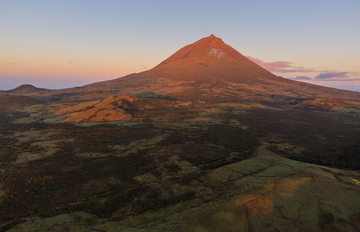 Aerial view of Lagoa do Capitão at sunrise with Mount Pico in the background, taken on Pico Island in the Azores. The soft morning light reveals the lake’s reflections and the volcanic peak.