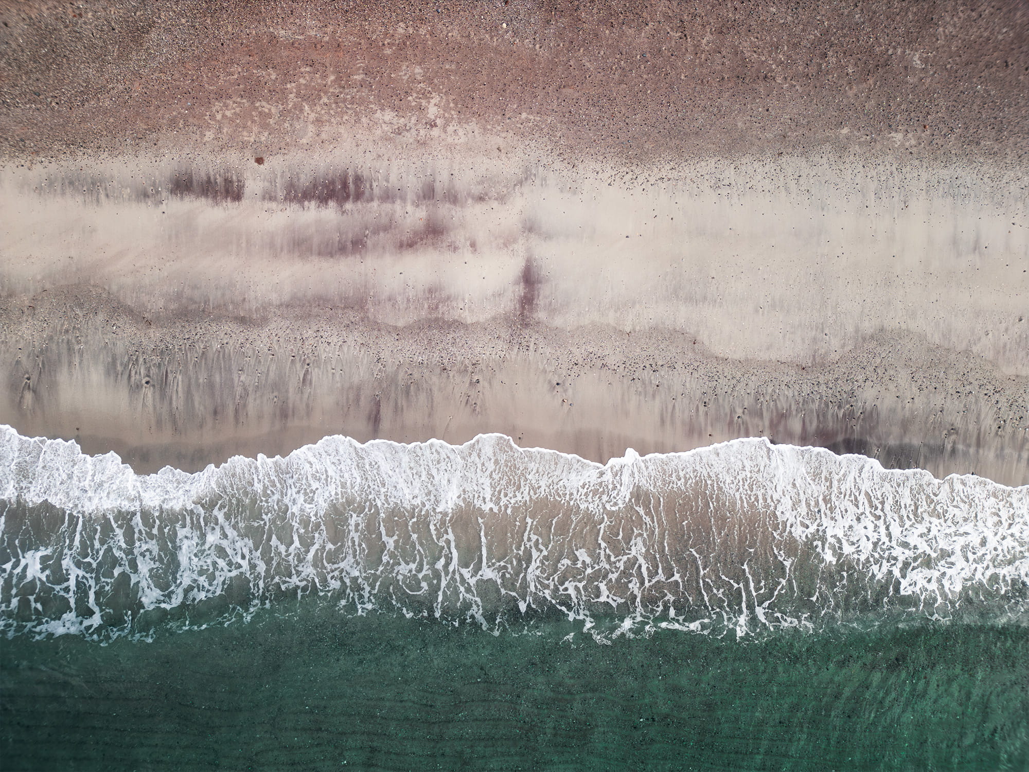 Aerial view of Mjelle Beach near Bodø, Norway, showing pink sand, turquoise water and waves along the Arctic coastline in Northern Norway.
