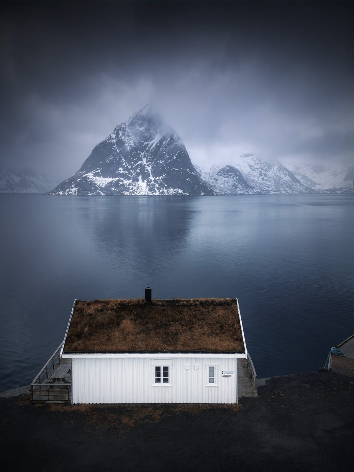 White house in Sakrisøy, Lofoten Islands, Norway, captured with a drone in moody weather with dark tones and soft Arctic light