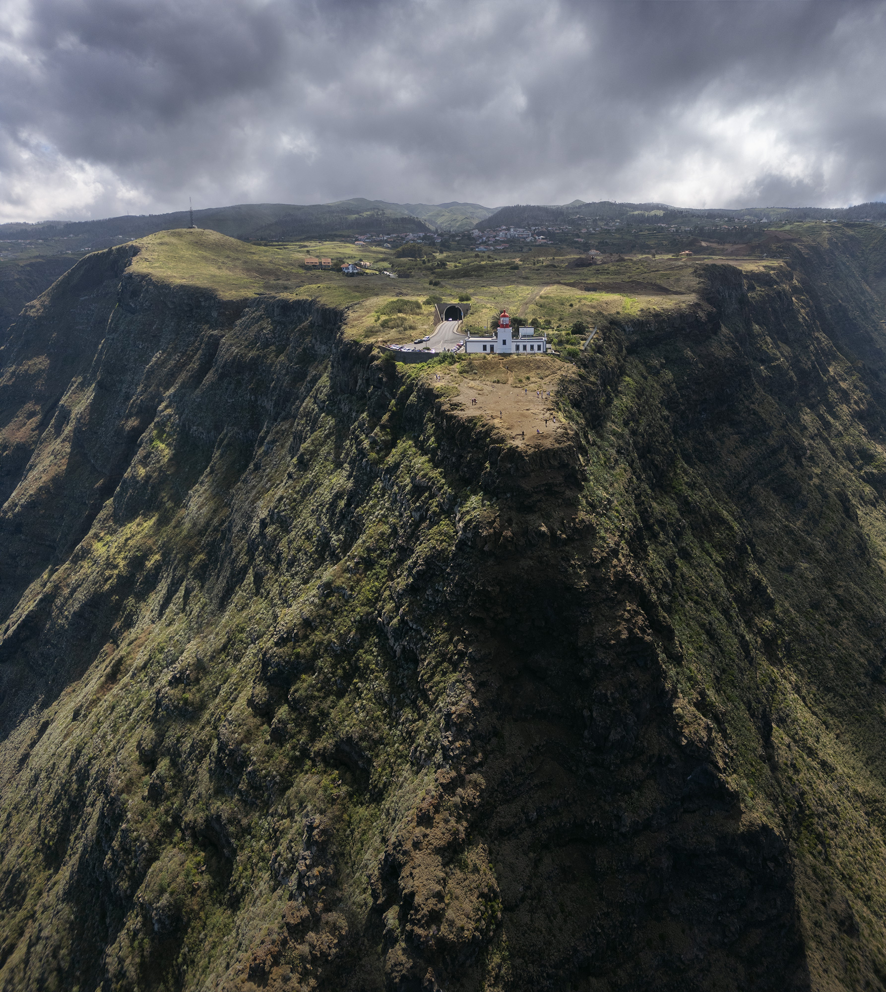 Aerial view of a lighthouse on top of a cliff in Madeira, Portugal, overlooking dramatic coastal landscapes under moody clouds