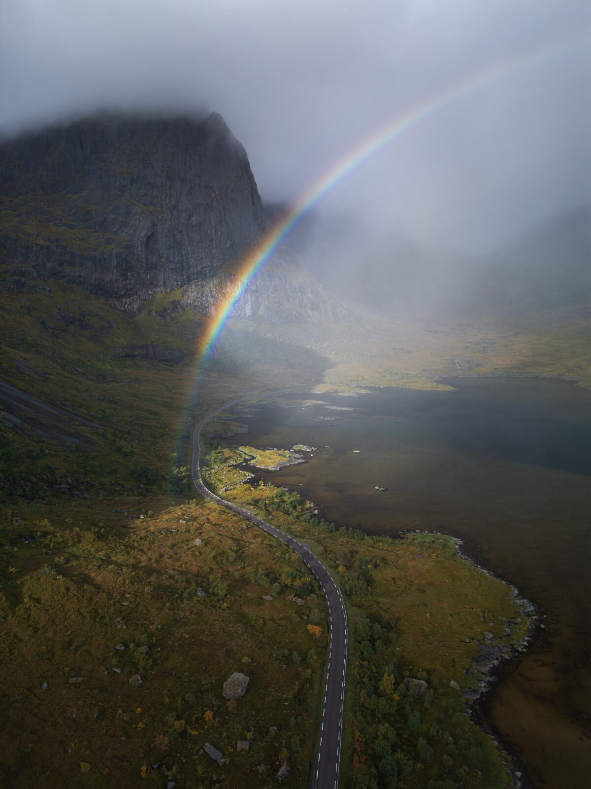 Rainbow over the road near Kilan in Flakstad, Lofoten Islands, Norway, with mountains and dramatic sky in Northern Norway.