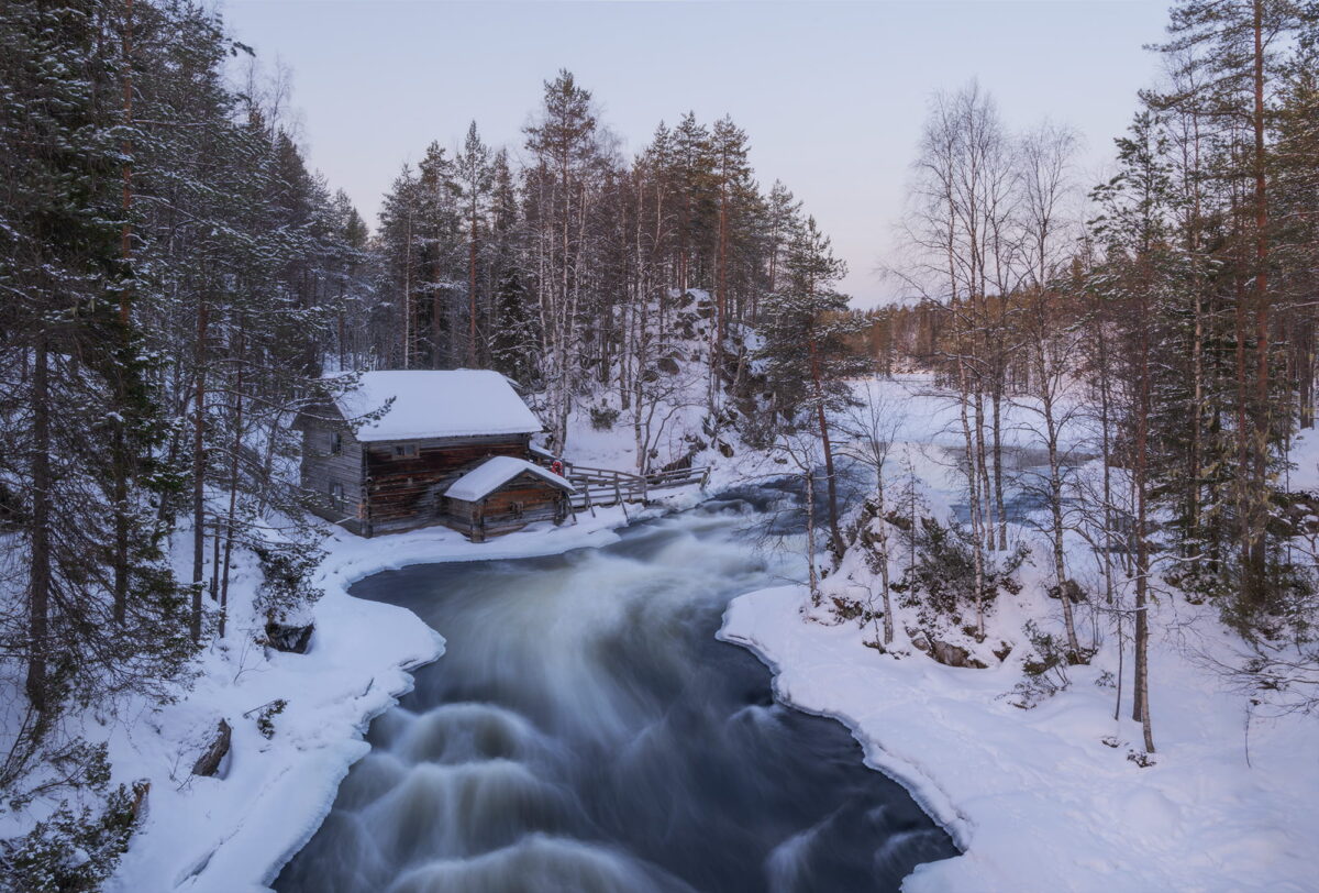 Myllykoski Rapids in Finnish Lapland with a wooden cabin and flowing river in winter, long exposure landscape photography in Finland.