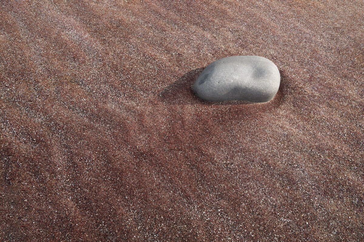 Close-up of pink sand at Mjelle Beach near Bodø, Norway, with a smooth stone on the colorful sand, Northern Norway landscape detail.