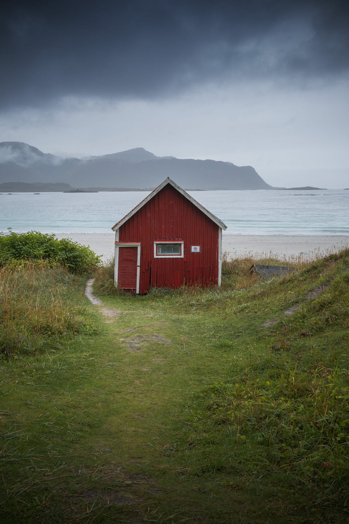 Red cabin on Ramberg Beach with mountains and stormy sky, Lofoten Islands, Norway