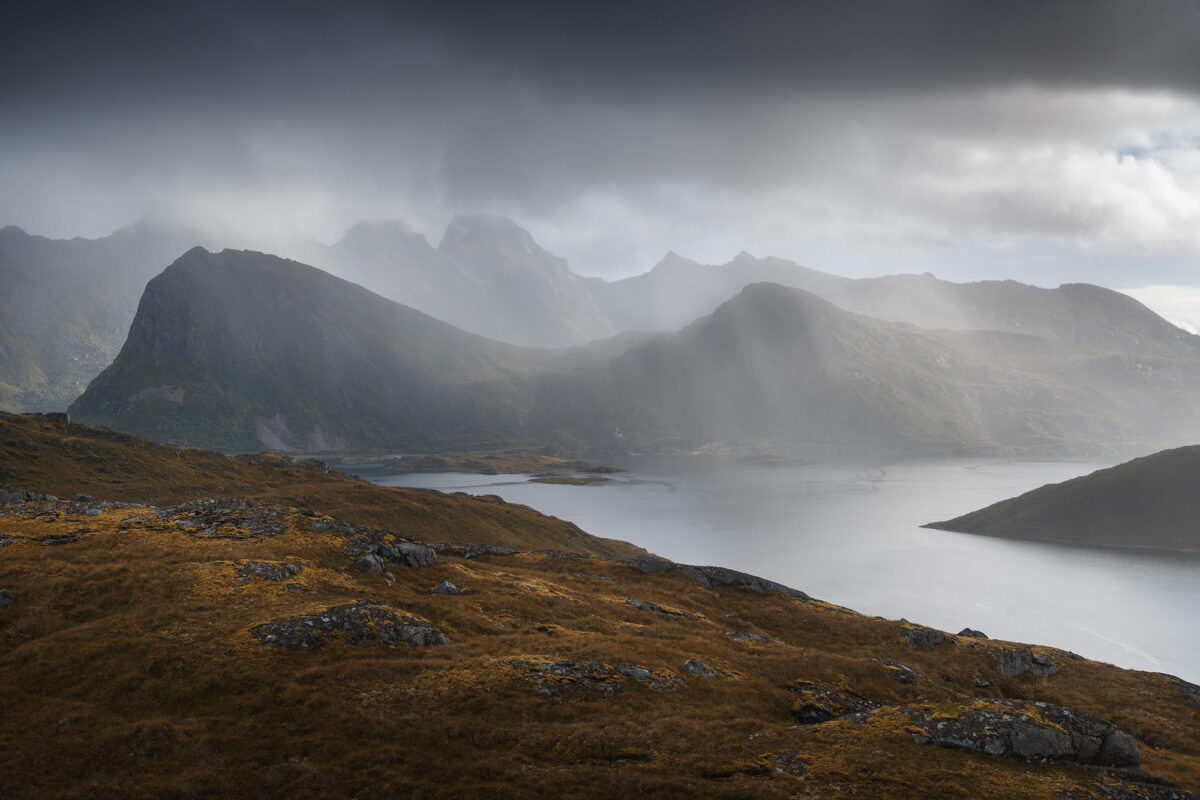 Moody landscape in the Lofoten Islands seen on the hike to Kvalvika Beach, with dramatic light rays breaking through clouds above fjords and mountains.