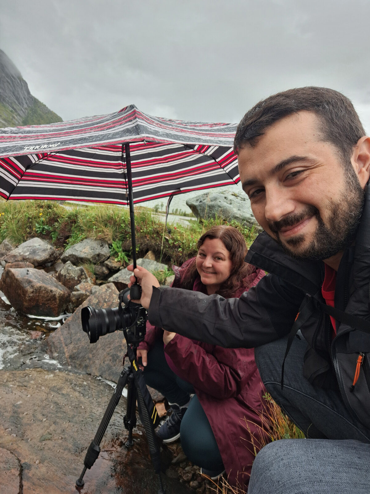 Swiss landscape photographer with her boyfriend under an umbrella at Molneva-fossen waterfall in the rain, Lofoten Islands, Norway