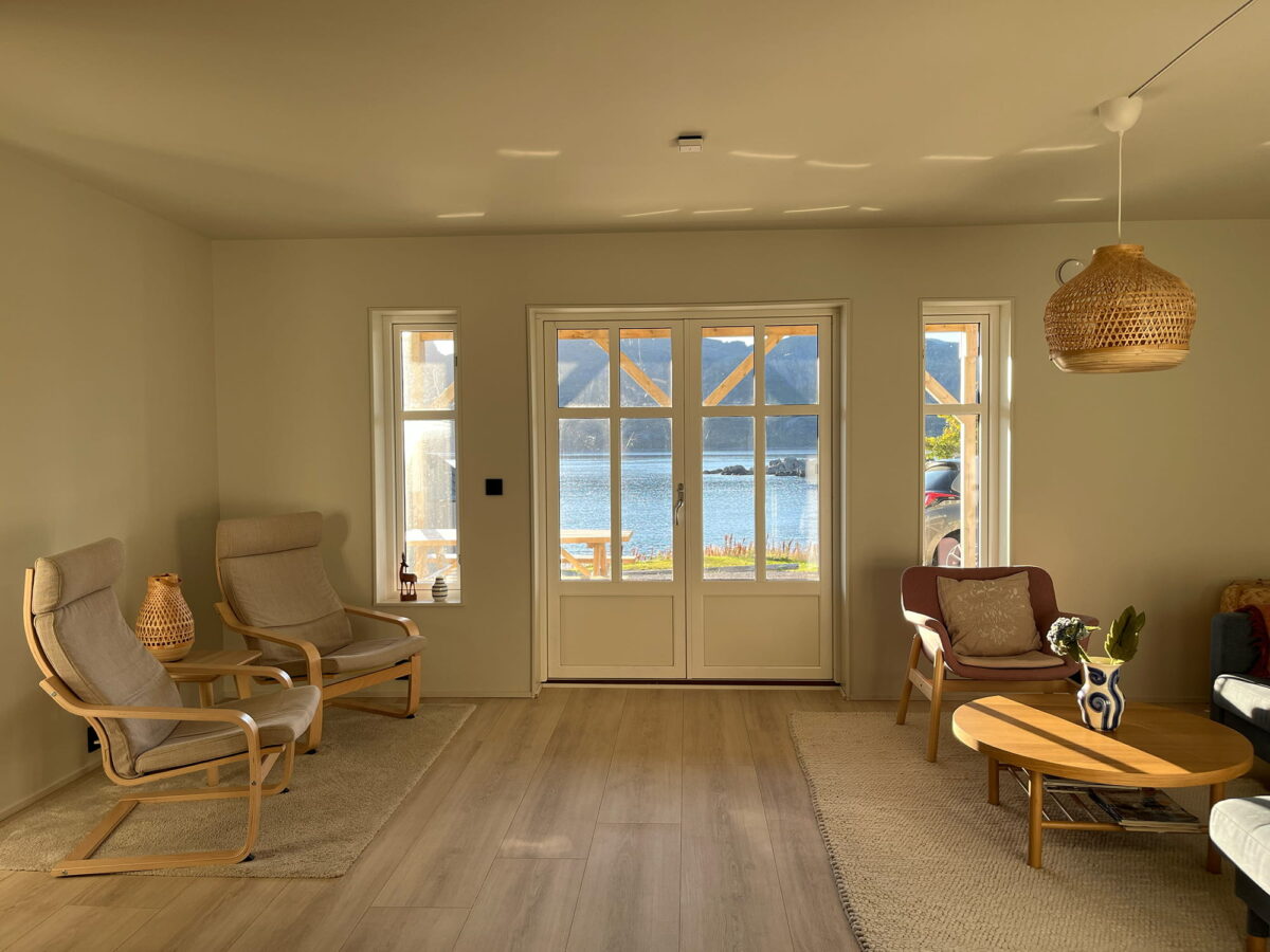Cozy living room in an apartment in central Lofoten near Gravdal, with two armchairs, a wooden table and large windows overlooking the sea and mountains.
