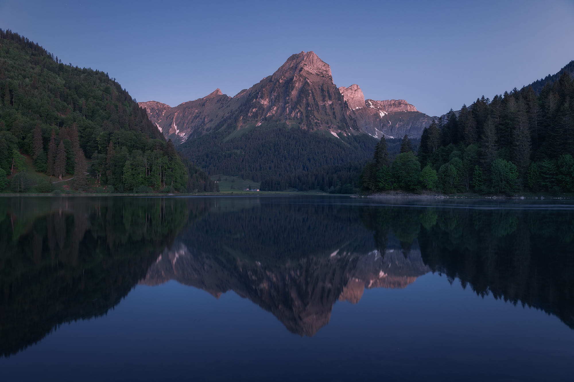 Blue hour landscape photography at Obersee in the Canton of Glarus, Switzerland, featuring a calm mountain lake with perfect reflections of the surrounding alpine peaks and forest under soft morning light.