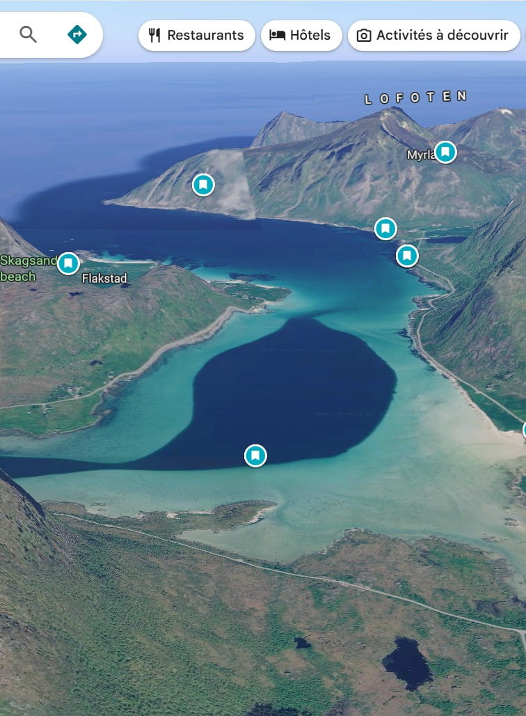 Google Maps 3D view of a lagoon near Flakstad in the Lofoten Islands, Norway, showing a large dark-blue shape surrounded by turquoise shallow waters that inspired a planned drone photography composition.