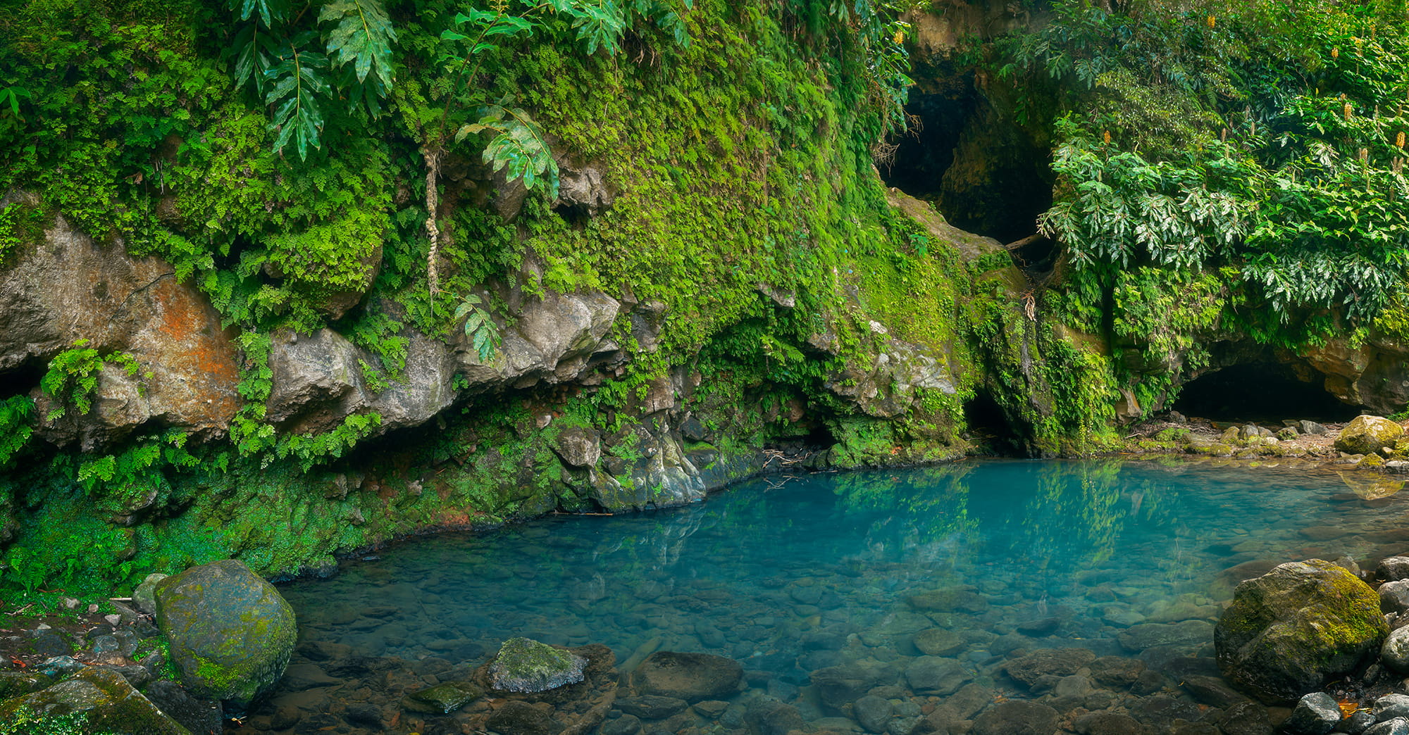 Fine art landscape photograph of Poço Azul on São Miguel Island, Azores, featuring a crystal-clear blue pool surrounded by lush volcanic rainforest and moss-covered cliffs.