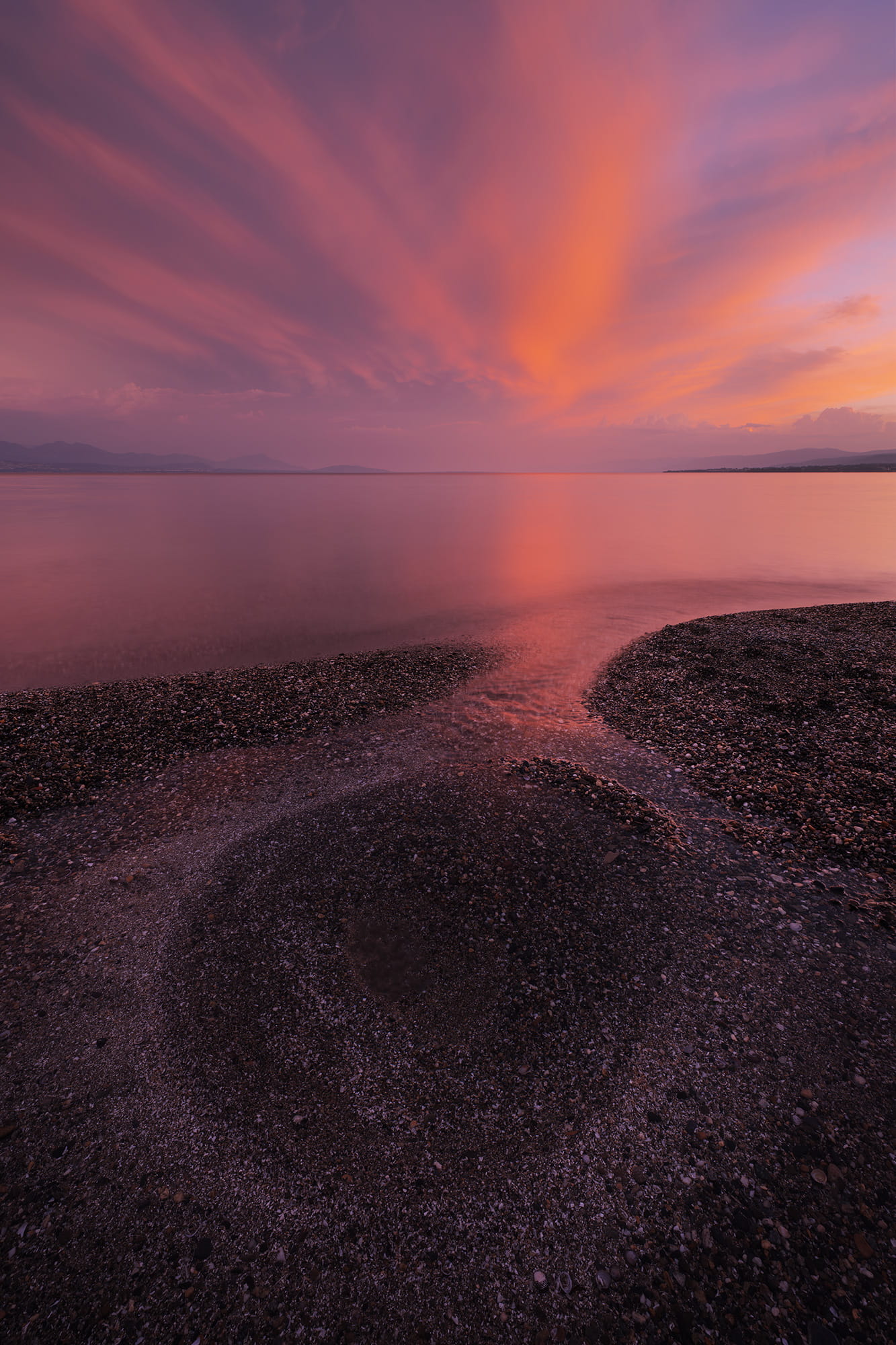 Wide-angle landscape photograph of a summer sunset over Lake Geneva in St-Sulpice near Lausanne, Switzerland, with dramatic pink clouds reflected on calm water.
