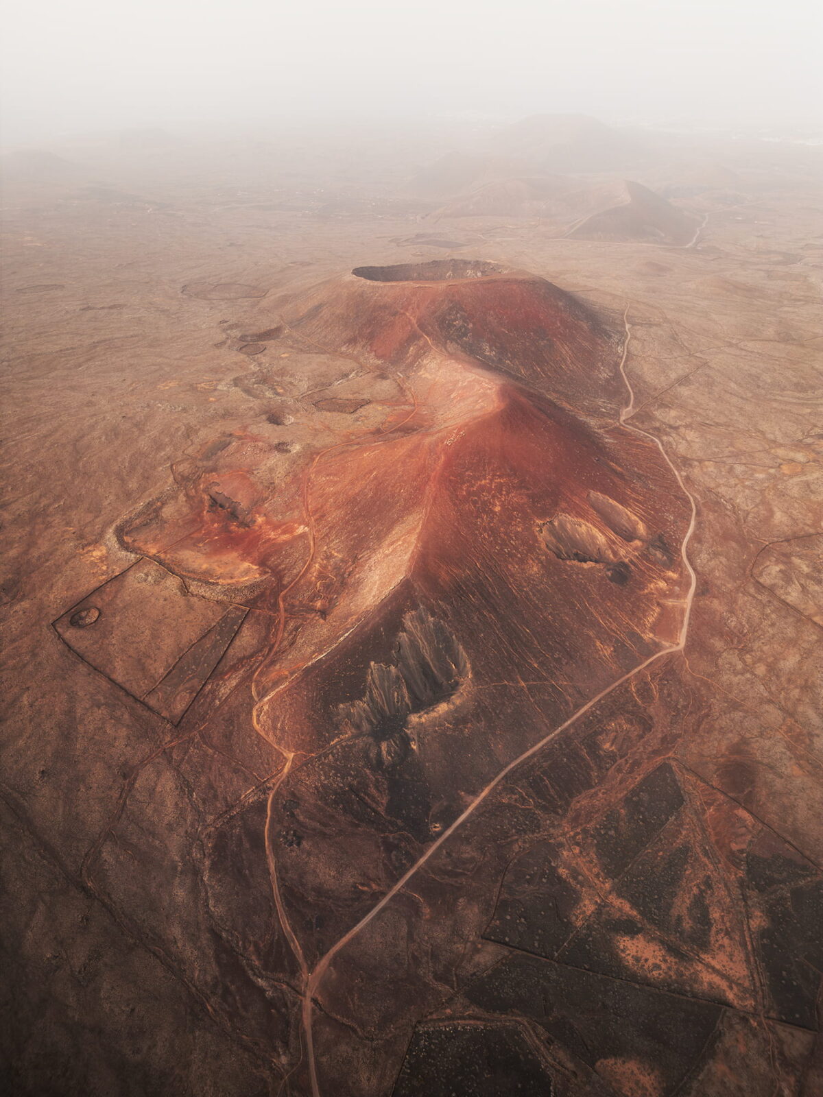 Drone view of Calderón Hondo and the volcanic landscape of northern Fuerteventura, with red volcanic cones emerging through atmospheric haze in the Canary Islands.