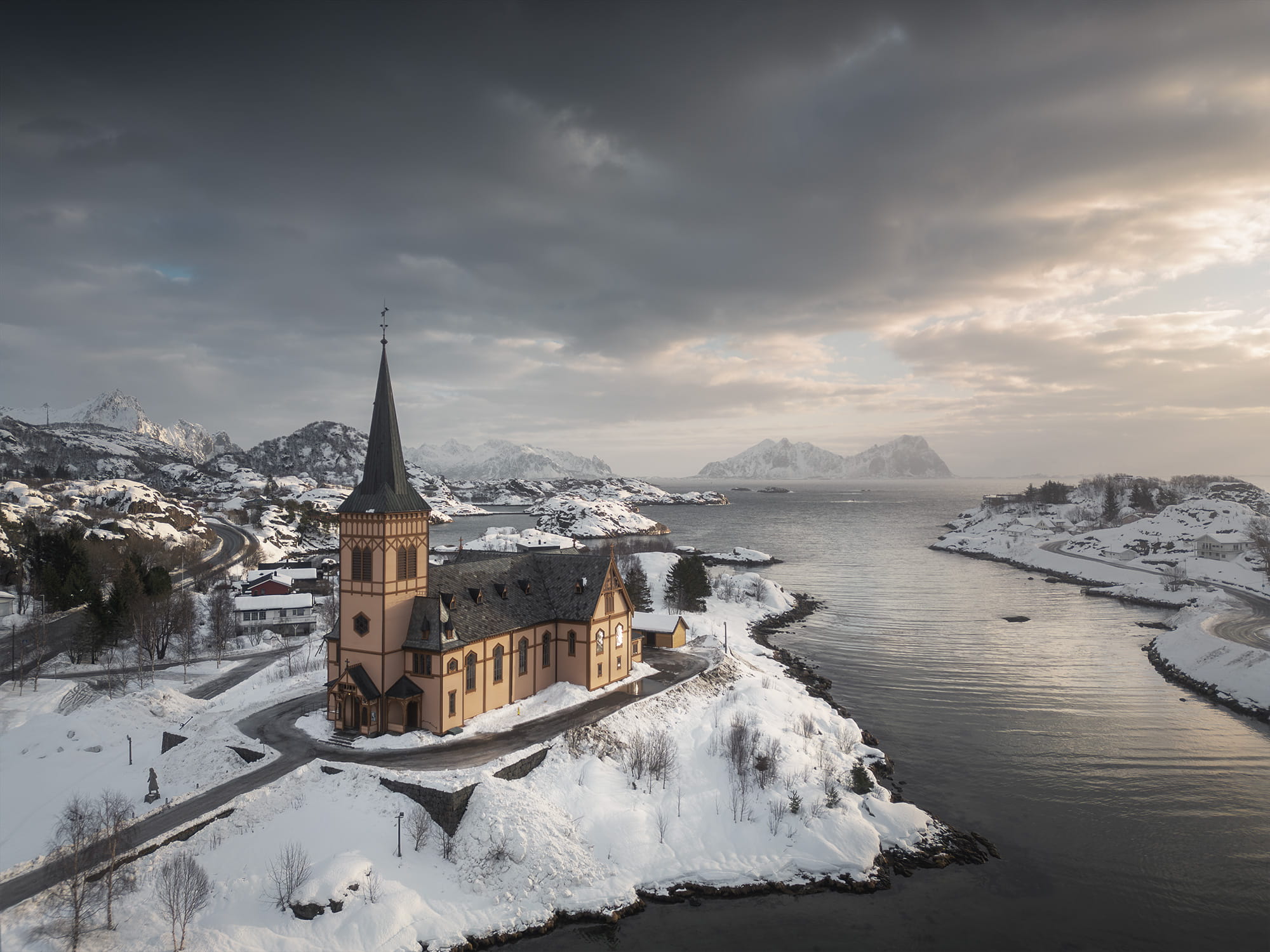 Winter aerial view of Kabelvåg Church surrounded by snow-covered landscapes and mountains along the Norwegian Sea in the Lofoten Islands, Norway.