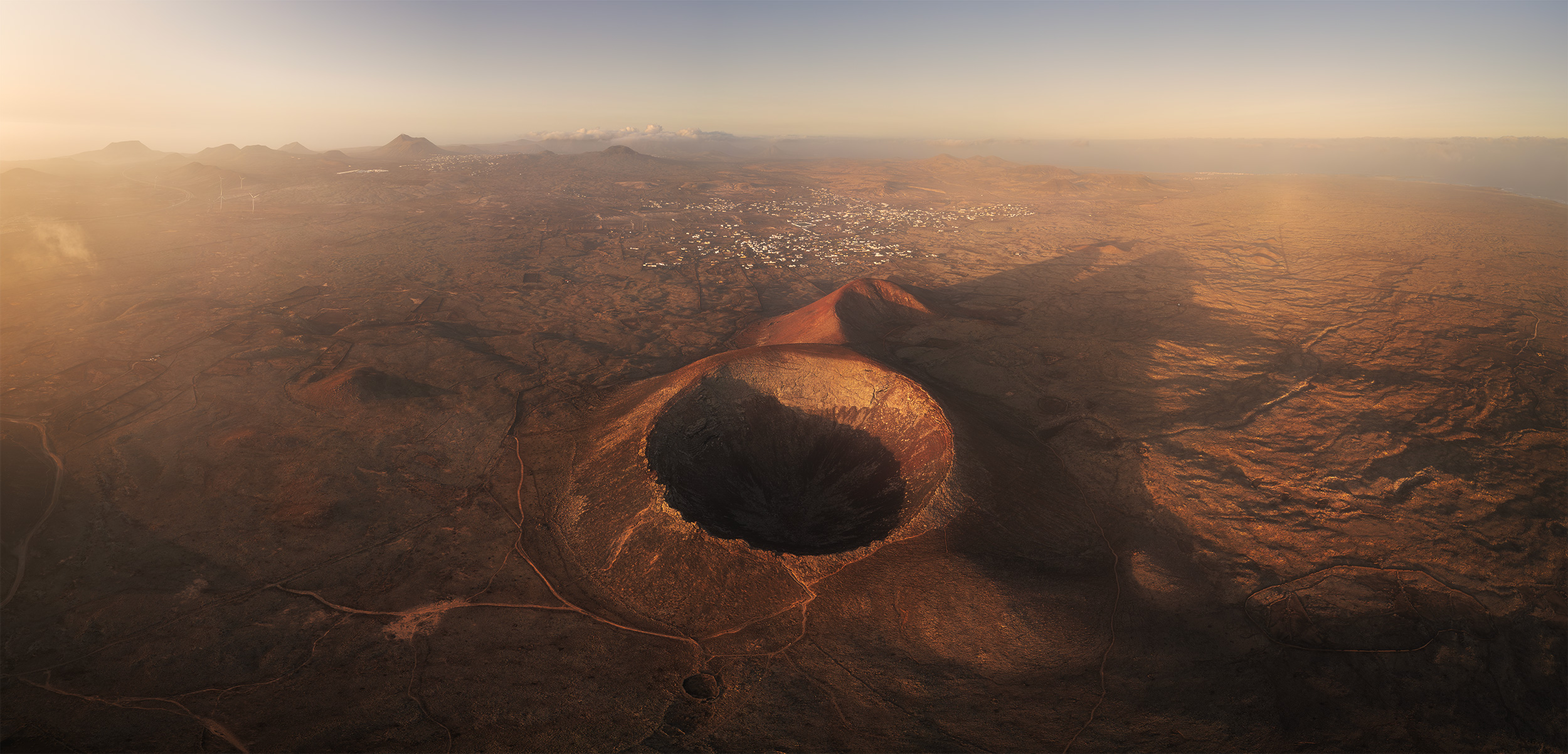 Drone panorama of Calderón Hondo volcano and its perfectly shaped crater at golden hour, overlooking the volcanic landscape of northern Fuerteventura, Canary Islands.