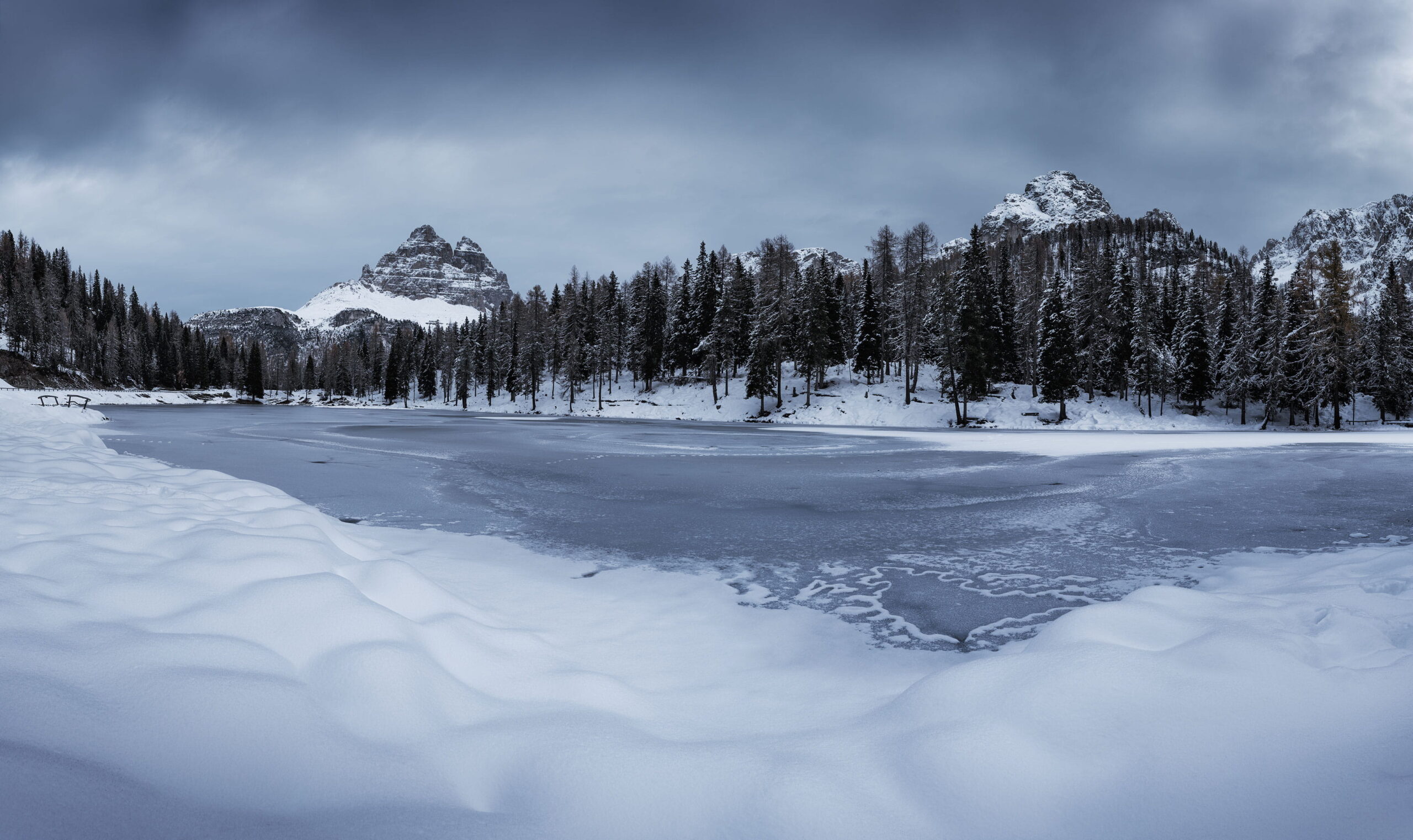 Winter landscape of frozen Lago d’Antorno in the Italian Dolomites, surrounded by snow-covered mountains and pine forest in November.