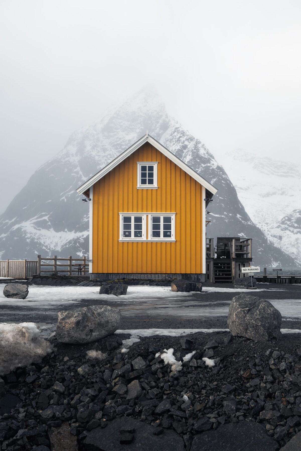 Traditional yellow wooden house in Sakrisøy, Lofoten Islands, Norway, framed by a snow-covered mountain disappearing into the winter mist.