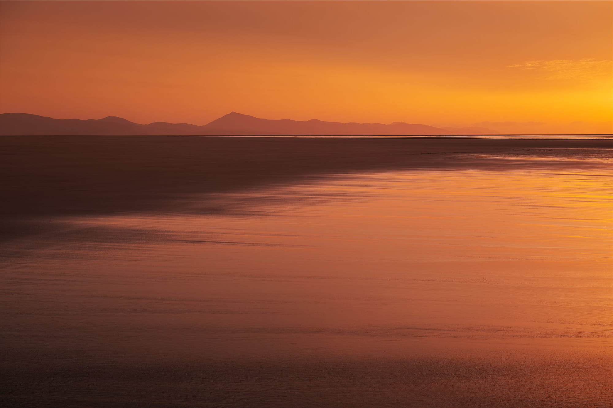 Sunrise over Sotavento Beach in Fuerteventura, Canary Islands, with golden light reflecting across the shallow water and distant volcanic mountains.