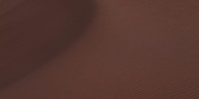 Minimalist landscape photography of a full moon rising above a rippled sand dune in Fuerteventura, Canary Islands, with warm reddish sand and a soft pink sky creating a peaceful atmosphere.